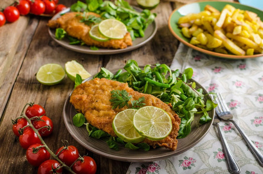 Delicious chicken cutlet served with fresh salad, lime slices, and a sprinkle of herbs. Cutlet vs schnitzel debate: Which one is your favorite?