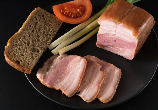 A plate with slices of salo, traditional Ukrainian bacon, served with bread, tomato, and green onions. Perfect for a classic salo recipe.